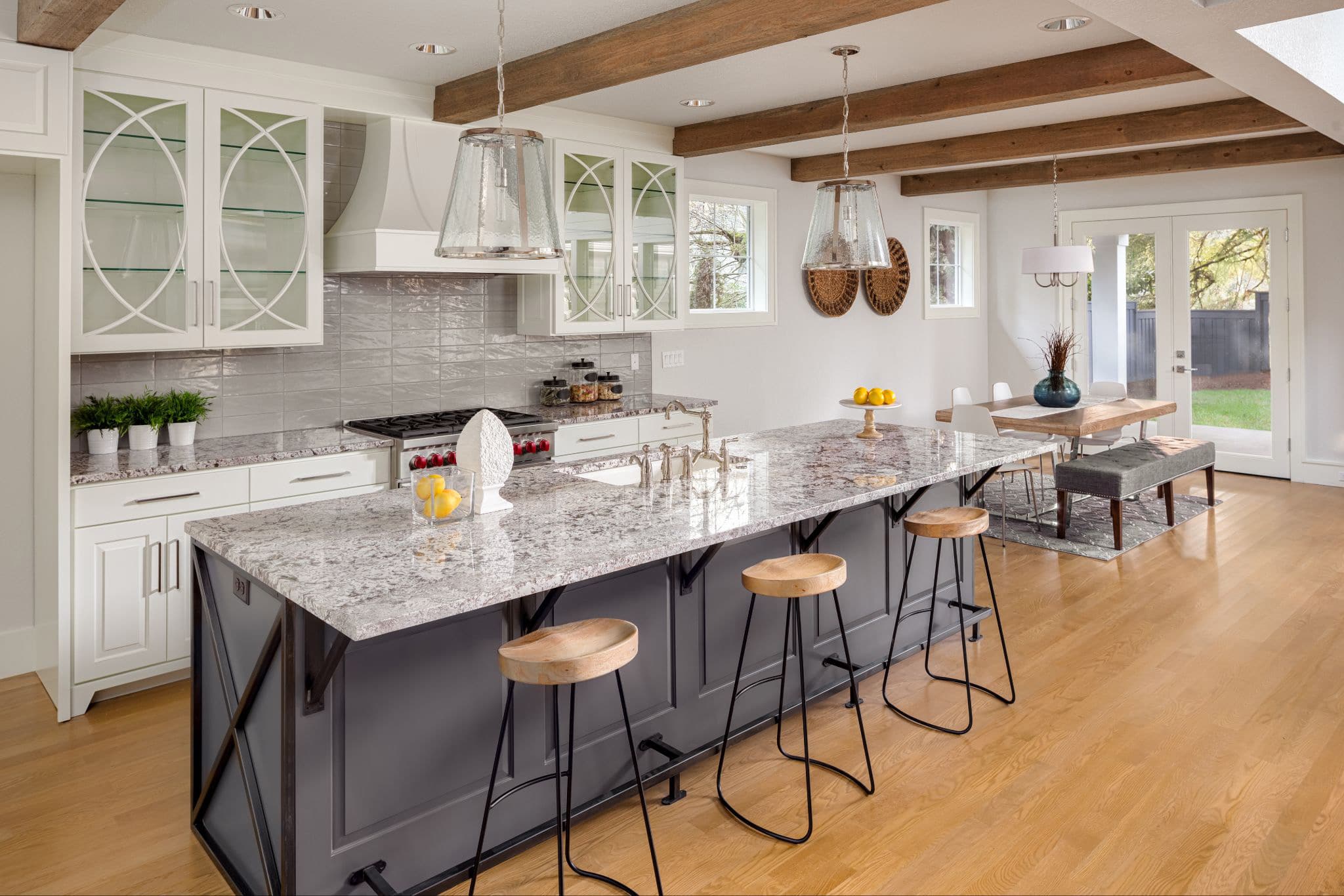 A-spacious,-modern-kitchen-with-a-large-gray-island,-granite-countertops,-bar-stools,-and-exposed-wooden-ceiling-beams.