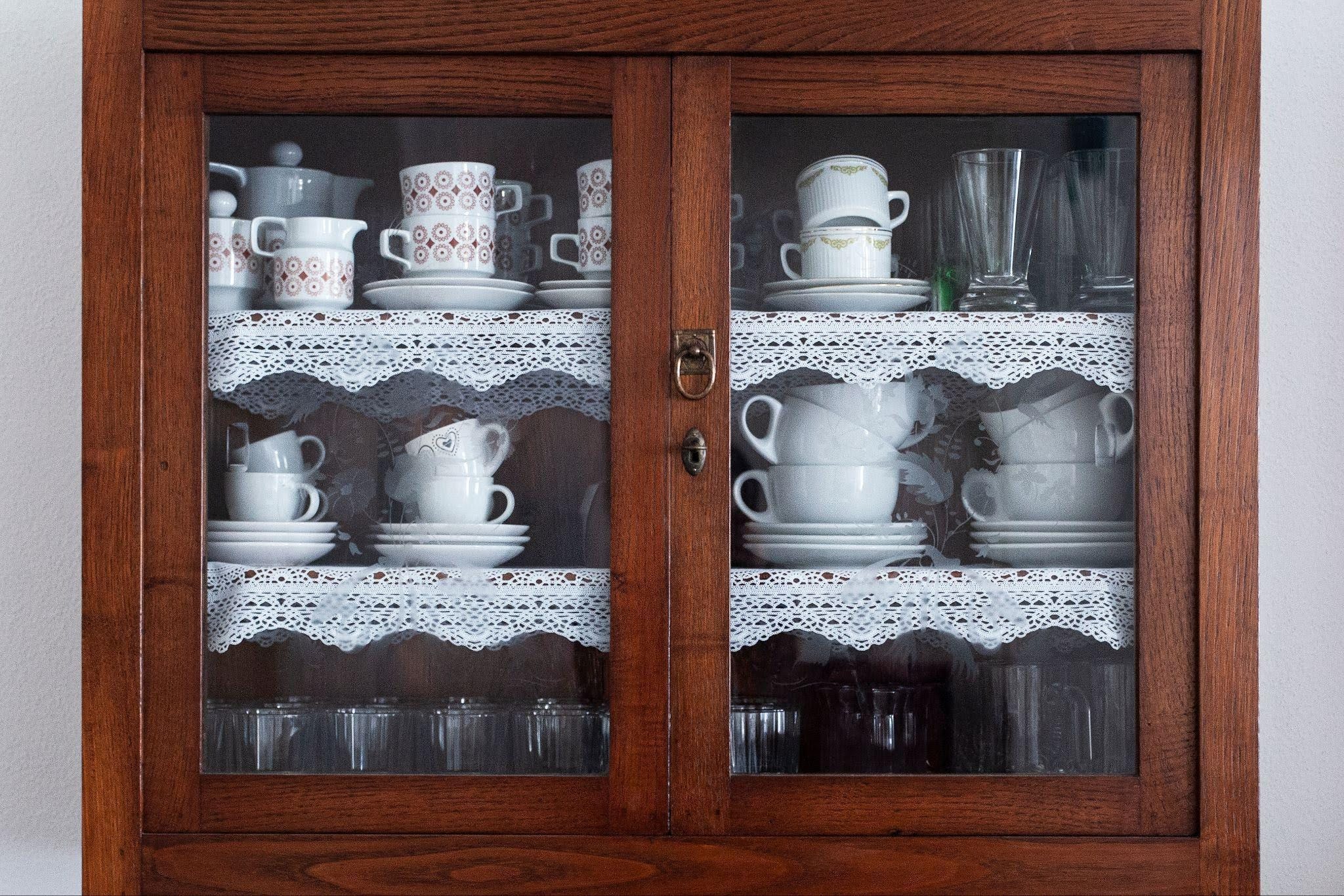 A wooden cabinet filled with various cups and saucers showcasing their designs on open shelves