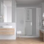 A modern bathroom with wooden floor, white walls, contemporary shower enclosure, and glass frame shower.