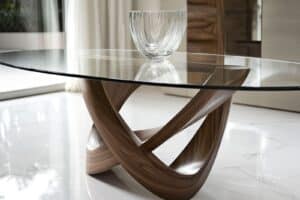 Modern glass-top coffee table with a wooden twisted base and a glass bowl centerpiece on a marble floor.