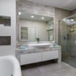 Modern bathroom with vessel sink, large mirror, glass shower, white tub, and neutral tile palette.