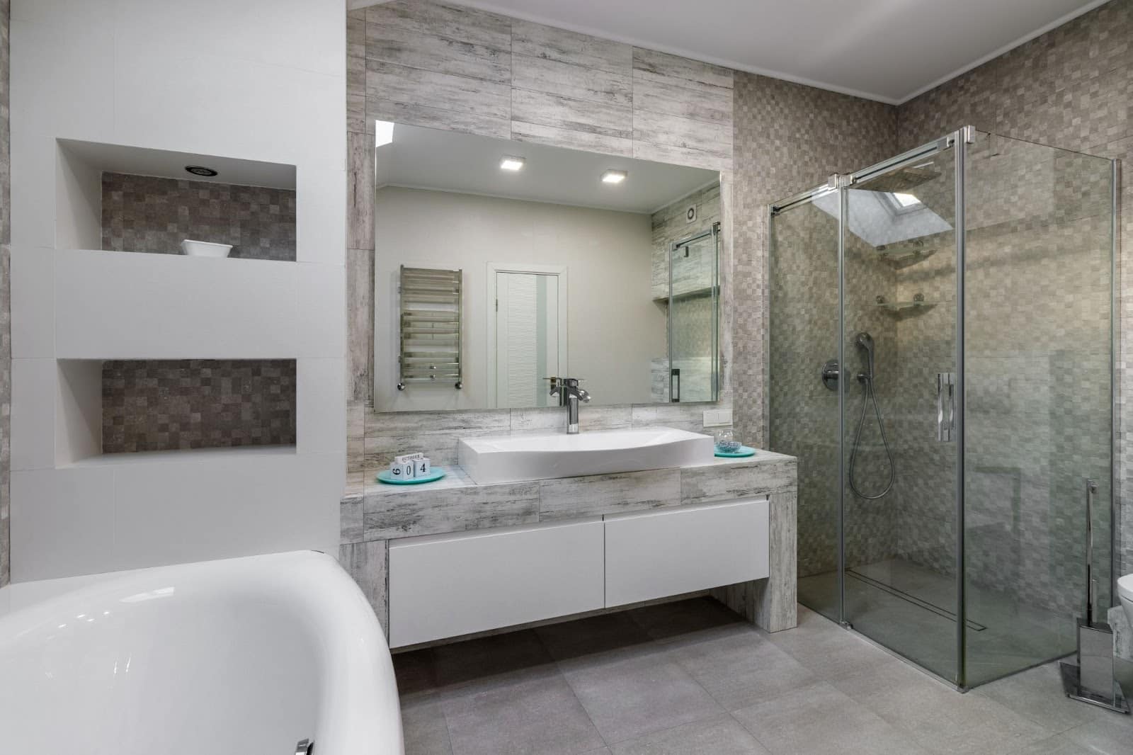 Modern bathroom with vessel sink, large mirror, glass shower, white tub, and neutral tile palette.